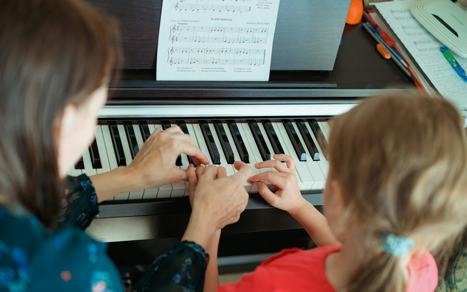 A teacher guiding a young student’s hands at the piano